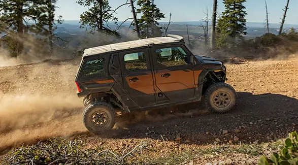 Side profile of a 2027 Polaris XPEDITION ADV 5 NorthStar side-by-side climbing up a dusty hill.