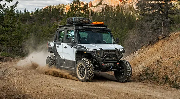 A rider cornering on a tight trail in the enclosed cab of a 2027 Polaris XPEDITION XP 5 NorthStar side-by-side.